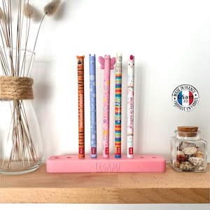 May include: A pink pen holder with five colorful pens. The pens have animal and whimsical designs, including a tiger, butterfly, and unicorn. The text on the pens reads "GREAT ADVENTURES", "WE ARE HERO HOORAY!", "YOU ARE BEAUTIFUL", "NO PROBLEMA", and "BELIEVE IN MAGIC".