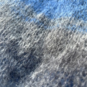 May include: Close-up of a soft, fuzzy fabric with a blue and grey colour gradient. The fabric has a textured, woven appearance.