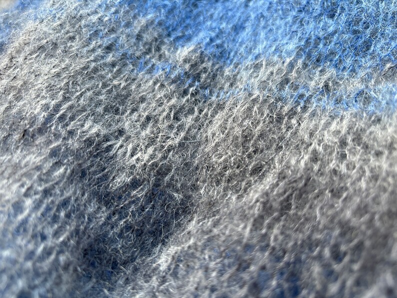May include: Close-up of a soft, fuzzy fabric with a blue and grey colour gradient. The fabric has a textured, woven appearance.