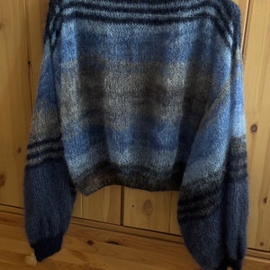 May include: A blue, grey and black striped knitted jumper with a wide, boat neck and long sleeves. The jumper has a relaxed fit and a cropped length.