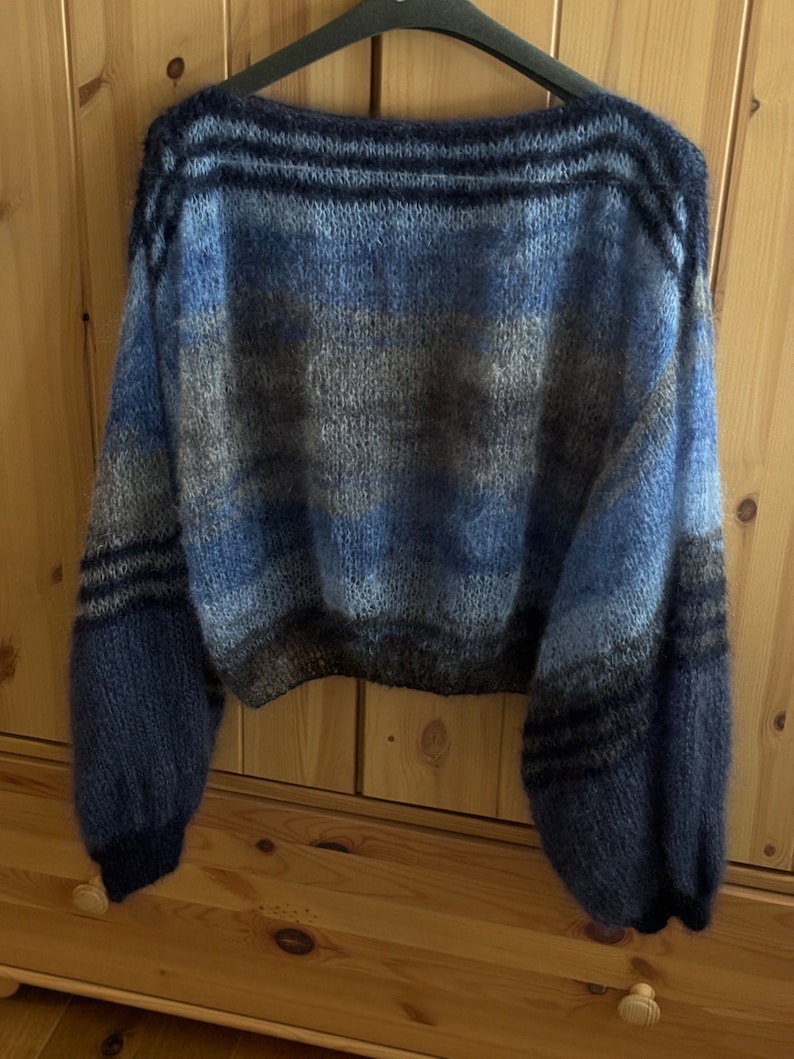 May include: A blue, grey and black striped knitted jumper with a wide, boat neck and long sleeves. The jumper has a relaxed fit and a cropped length.