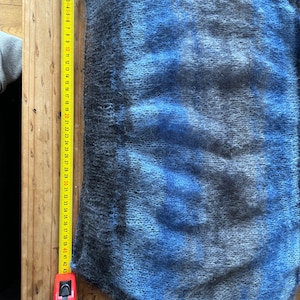 May include: A blue and grey fuzzy sweater with a measuring tape next to it. The tape measures 109 cm.