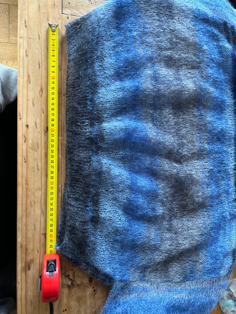 May include: A blue and grey fuzzy sweater with a measuring tape next to it. The tape measures 109 cm.