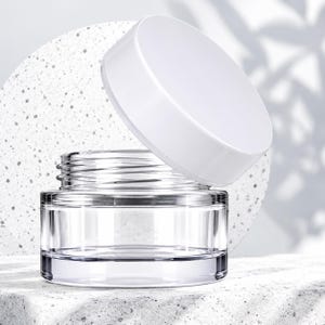 May include: A clear glass cosmetic jar with a wide, smooth, white screw-top lid. The jar features a thick, transparent base with visible threading at the neck for the lid, designed for holding creams or other skincare products.