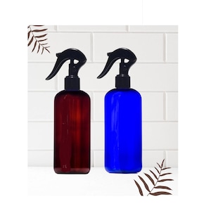 Peut inclure: Deux flacons pulvérisateurs en plastique avec des gâchettes noires. Un flacon est brun et l'autre est bleu.