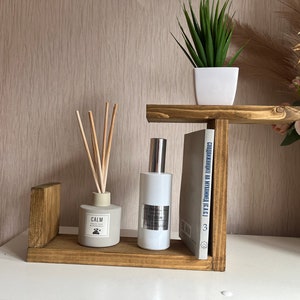 May include: A wooden shelf unit with two shelves, a book, a diffuser, and a spray bottle. The diffuser is labelled "Calm".