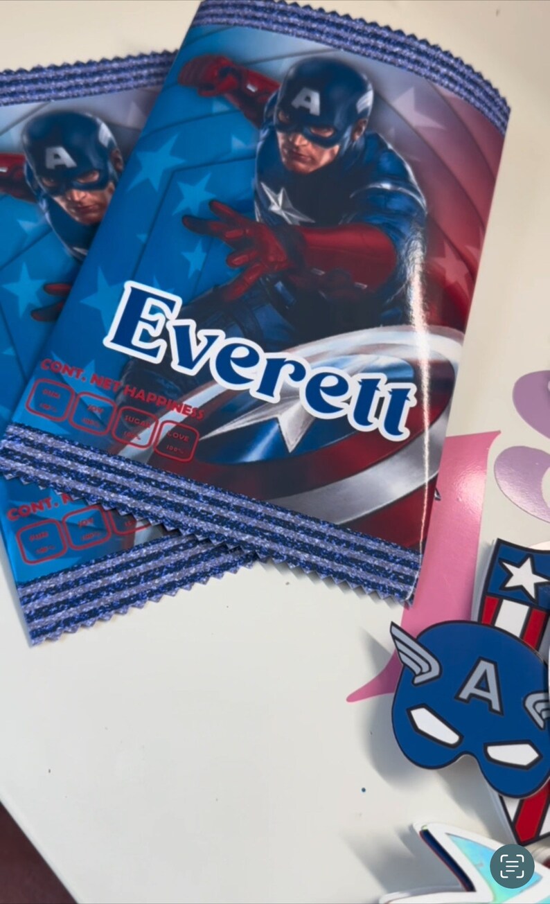 May include: Two blue and red Captain America themed party favour bags with the name Everett printed on the front. The bags have a blue and silver glitter trim.