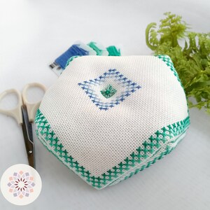 Octagonal embroidered pin cushion with sea wave motifs in varying shades of green and blue, complemented by pearly sea foam-colored thread ornaments. Back side view of a less profuse embroidering.