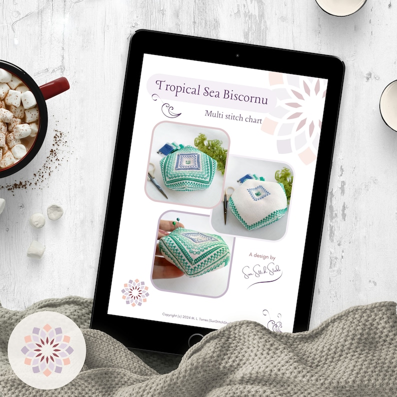 Image displaying the document's initial page with title and pictures, shown in a tablet on a white table surrounded by a blanket and a cup of cocoa with marshmallows.
