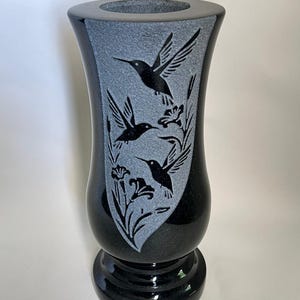 May include: Black and gray vase with a flared top and a pedestal base. The vase features a gray panel with etched hummingbirds and floral designs. The vase is approximately 10 inches tall.