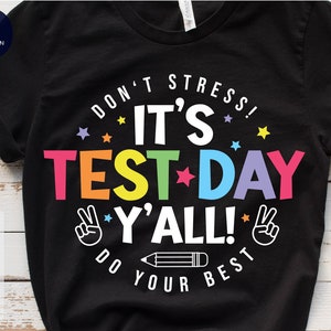 May include: Black t-shirt with a rainbow colored graphic that says "Don't Stress! It's Test Day Y'all! Do Your Best".