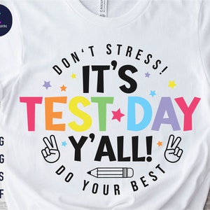 May include: White t-shirt with a colorful graphic that says "Don't Stress! It's Test Day Y'all! Do Your Best". The graphic includes stars, a pencil, and peace signs.