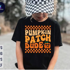 May include: Black t-shirt with the text "PUMPKIN PATCH DUDE" in orange and white, featuring a pumpkin wearing sunglasses. The shirt has a checkered pattern border and is suitable for fall or Halloween.