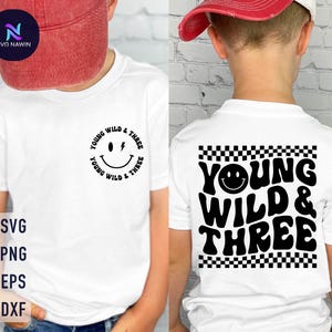 Pode incluir: Duas camisetas brancas com um design gráfico preto. O design apresenta um rosto sorridente com um raio e o texto "Young Wild & Three". Uma camiseta tem o design em uma caixa quadriculada, a outra tem o design em um círculo.
