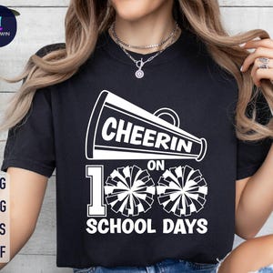 May include: Black t-shirt with a white graphic of a megaphone with the text "Cheer on 100 School Days" and two white cheerleading pom-poms.