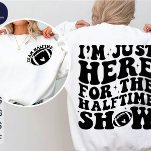 Può includere: Felpa bianca con testo nero che recita "I'm Just Here For The Halftime Show" e una grafica di un pallone da calcio. Il testo è in uno stile di font retrò.
