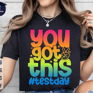 Puede incluir: Camiseta negra con un gráfico de arcoíris que dice "You got this #testday".