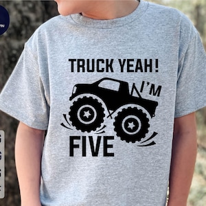 Può includere: Una maglietta grigia con una grafica nera di un monster truck e il testo "Truck Yeah! I'm Five".
