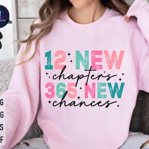 May include: Pink sweatshirt with the text "12 NEW chapters 365 NEW chances" in colorful, distressed lettering.