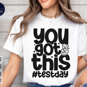 May include: White t-shirt with black text that reads "You got this #testday" with a peace sign graphic.