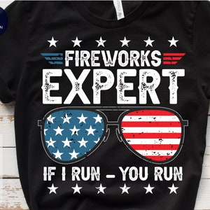 May include: Black t-shirt with a white graphic design featuring a pair of sunglasses with an American flag pattern and the text "FIREWORKS EXPERT IF I RUN - YOU RUN".