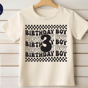 May include: A white t-shirt with a black and white checkered pattern and the text "Birthday Boy" repeated multiple times. The number "3" is in the center of the design.