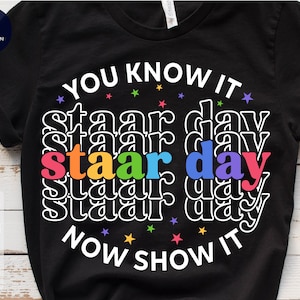 May include: Black t-shirt with the text "YOU KNOW IT" and "STAAR DAY" repeated multiple times in rainbow colors. The text "NOW SHOW IT" is below the rainbow text.
