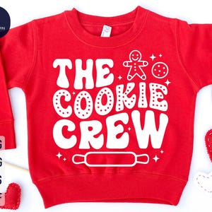 May include: Red sweatshirt with white text that says "The Cookie Crew" with a gingerbread man and a cookie graphic.