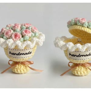 Könnte beinhalten: Gehäkelte Ringbox in Cupcake-Form, verziert mit rosa und grünen Häkelblumen. Die gelbe Box hat eine weiße Spitzenborte und ein Band mit der Aufschrift "handmade". Eine Box ist geöffnet und zeigt einen Ring.