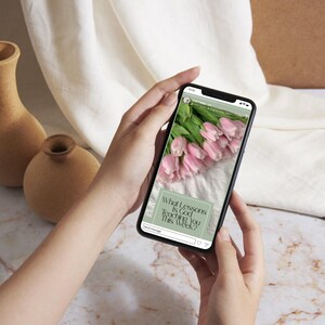 K&ouml;nnte beinhalten: Ein schwarzes Smartphone, das einen Social-Media-Beitrag mit einem Strau&szlig; hellrosa Tulpen und einem salbeigr&uuml;nen Textfeld mit den Worten What Lessons Is God Teaching You This Week? anzeigt. Der Bildschirm zeigt zudem ein kleines Profilsymbol.