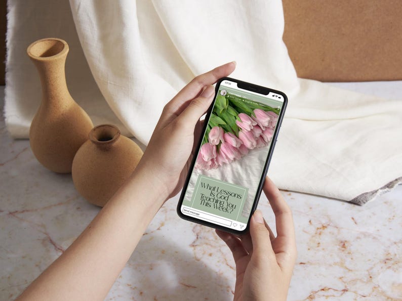K&ouml;nnte beinhalten: Ein schwarzes Smartphone, das einen Social-Media-Beitrag mit einem Strau&szlig; hellrosa Tulpen und einem salbeigr&uuml;nen Textfeld mit den Worten What Lessons Is God Teaching You This Week? anzeigt. Der Bildschirm zeigt zudem ein kleines Profilsymbol.