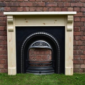May include: A wooden fireplace mantel with a black cast iron fireplace insert. The mantel is made of unfinished pine wood and has a simple design. The fireplace insert has a decorative arch and a grate.