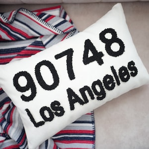 May include: White cushion with black embroidered text "90748 Los Angeles".