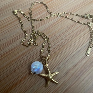 Könnte beinhalten: Eine goldene Kettenkette mit einem Mondstein-Anhänger und einem goldenen Seestern-Anhänger.