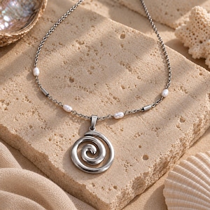 May include: A silver-toned necklace featuring a circular spiral pendant suspended from a delicate chain. The chain is accented with small, white, oval-shaped pearls and short, cylindrical silver-toned metal beads spaced evenly along the length.