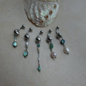 May include: Five curved barbell body jewellery pieces featuring silver-toned metal balls and dangling charms. The charms include small white pearls, iridescent abalone shell discs, and green stone beads attached with thin silver-coloured metal chains.