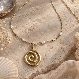 May include: A gold-toned necklace featuring a spiral pendant and a delicate chain accented with small, white, irregular-shaped pearls. The metal chain links are interspersed with smooth, cylindrical gold-toned beads between the pearls.