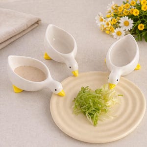 Puede incluir: Un juego de tres tazas de cerámica con un acabado mate moteado. Las tazas son en tonos crema, gris claro y gris oscuro. Cada taza tiene un diseño simple y minimalista, ideal para café o té.