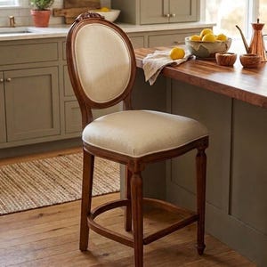 May include: A wooden bar stool with a dark brown finish, featuring a round backrest and a square seat both upholstered in a light beige fabric. The stool has four straight legs with decorative carvings and a curved support stretcher at the base.