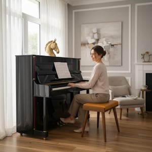 May include: A glossy black upright piano with a gold horse head sculpture on top and sheet music on the stand. A person in a beige long-sleeved top and tan trousers sits on a rectangular wooden bench with a tan cushion, playing the piano keys.