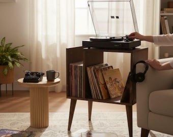 May include: A dark wood record player stand with four tapered legs, featuring open storage shelves filled with vinyl records. A black turntable with a clear dust cover sits on top. A pair of black headphones hangs from the side of the wooden unit.