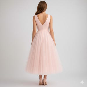 Op de afbeelding: Een lichtroze midi-jurk met een V-hals en een volle tule rok. De jurk heeft een getailleerd lijfje en een gedefinieerde taille. Het model draagt lichtroze hakken. De jurk is geschikt voor speciale gelegenheden.