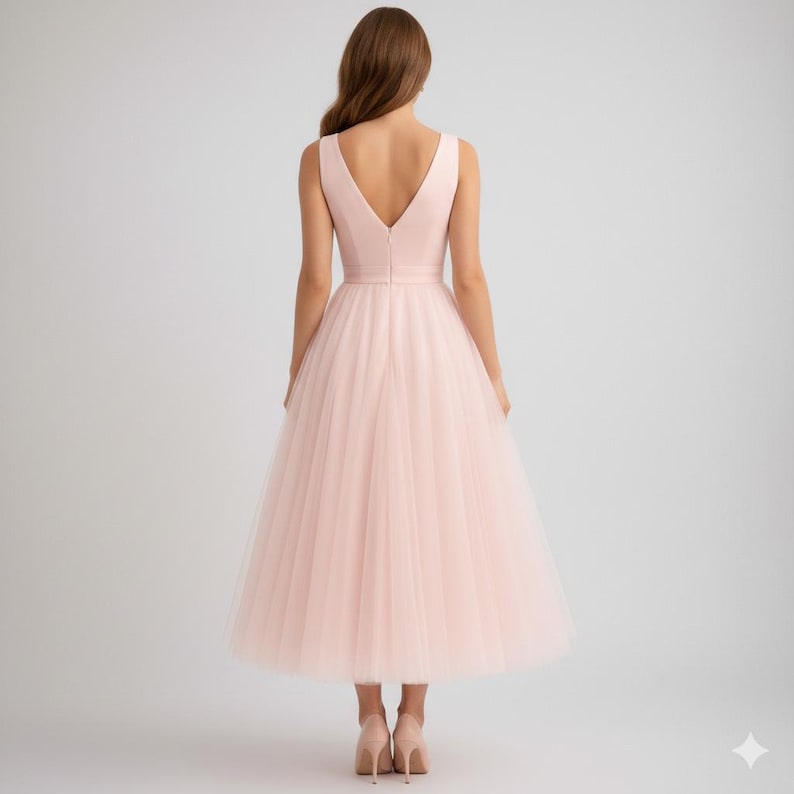 Op de afbeelding: Een lichtroze midi-jurk met een V-hals en een volle tule rok. De jurk heeft een getailleerd lijfje en een gedefinieerde taille. Het model draagt lichtroze hakken. De jurk is geschikt voor speciale gelegenheden.