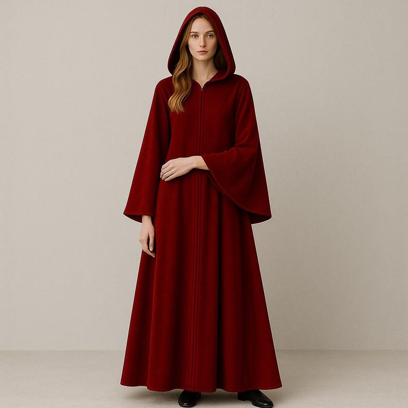 May include: A full-length, hooded cloak in a deep red hue. The cloak features a long, flowing design with wide sleeves and a front zipper closure. The hood is generously sized, and the garment appears to be made of a soft, warm fabric, suitable for cooler weather.