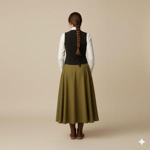 May include: A black vest over a white long-sleeve shirt, paired with an olive green skirt and brown boots. The skirt is a full, flowing style. The outfit is shown from the back.