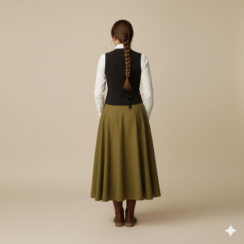 May include: A black vest over a white long-sleeve shirt, paired with an olive green skirt and brown boots. The skirt is a full, flowing style. The outfit is shown from the back.