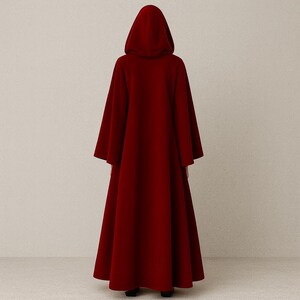 May include: A long, flowing, hooded cloak in a deep red color. The cloak has wide sleeves and a full skirt, creating a dramatic silhouette. The hood is large and covers the head, and the cloak appears to be made of a soft, heavy fabric.