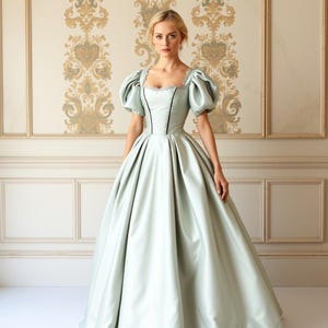May include: A woman wearing a light green satin ball gown with a black trim and puffed sleeves. The gown has a fitted bodice and a full skirt.