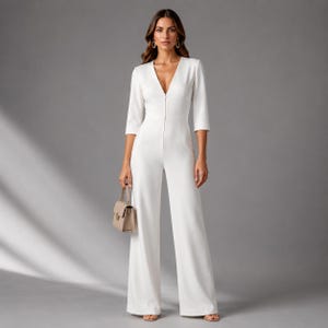 May include: A white jumpsuit with a V-neckline and wide-leg pants. The three-quarter sleeve jumpsuit has a tailored fit and a zipper closure. A small beige handbag is held in the hand. The model is wearing gold earrings and sandals.