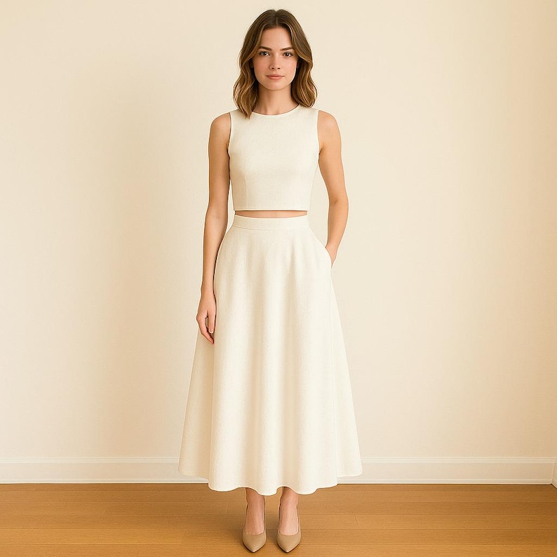 May include: A cream-colored two-piece outfit consisting of a sleeveless crop top and a midi-length skirt. The skirt has pockets and a flared silhouette. The outfit is paired with beige heels. The ensemble is suitable for formal occasions.